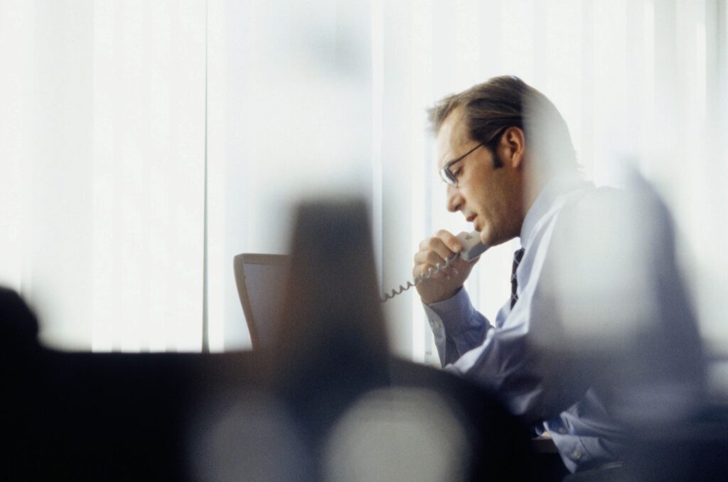 Man wearing glasses and a business shirt talking on a telephone while working